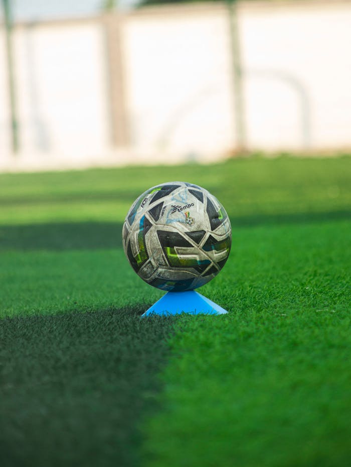 Soccer ball resting on teal cone on lush green field. Perfect for sports themes.